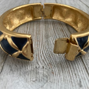 May include: Gold tone hinged bangle bracelet with a blue enamel design. The bracelet has a geometric pattern with a floral motif.