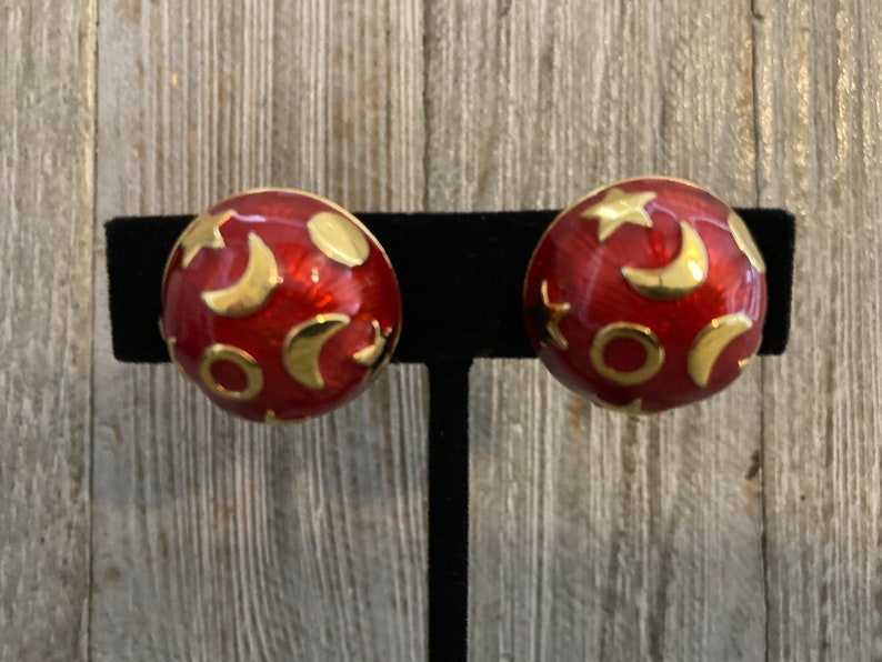 May include: A pair of red and gold earrings with a moon and star design.