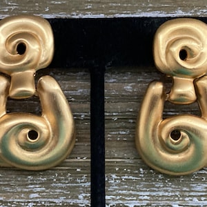 May include: A pair of gold-tone earrings with a swirl design. The earrings are in the shape of a door knocker.