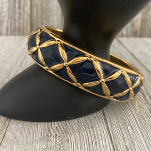 May include: A gold bangle bracelet with a navy blue enamel finish. The bracelet features a geometric pattern of gold leaves and dots.