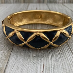 May include: A gold bangle bracelet with a blue enamel design. The enamel is in a quilted pattern with gold accents.