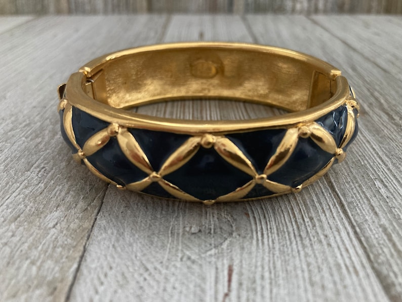 May include: A gold bangle bracelet with a blue enamel design. The enamel is in a quilted pattern with gold accents.