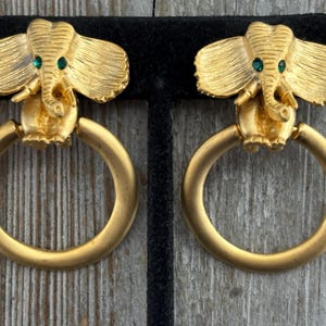 Può includere: Un paio di orecchini dorati a forma di batacchio con accenti di elefante in strass verdi.