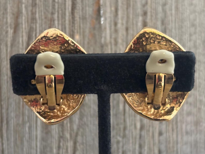Pu&ograve; includere: Un paio di orecchini vintage a clip. Ogni orecchino presenta un design a forma di diamante dorato con una superficie strutturata. Il meccanismo a clip &egrave; dorato con un cuscinetto color crema per il comfort.