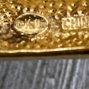 May include: Close-up of a gold-colored metal object with the text "OKUL" and "CHINA" stamped on it.