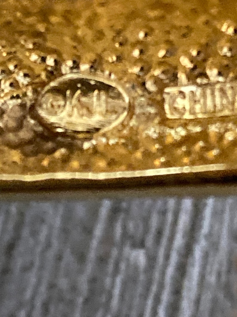 May include: Close-up of a gold-colored metal object with the text "OKUL" and "CHINA" stamped on it.