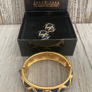 May include: A gold bangle bracelet with a blue enamel design and a matching pair of blue enamel earrings. The jewellery is in a black box with the text "Joan Rivers Classics Collection".