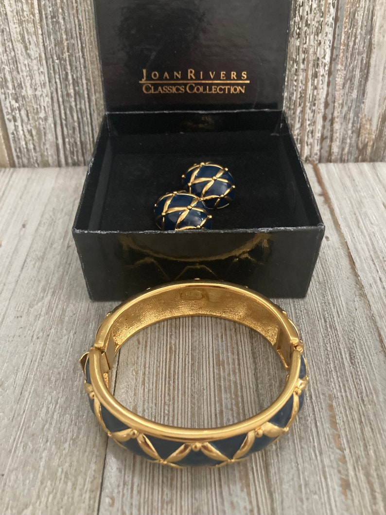 May include: A gold bangle bracelet with a blue enamel design and a matching pair of blue enamel earrings. The jewellery is in a black box with the text "Joan Rivers Classics Collection".