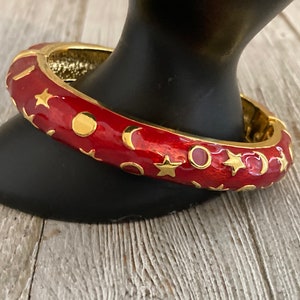 May include: Red enamel bangle bracelet with gold stars and crescent moons.