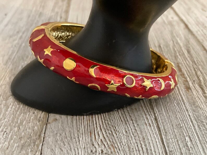 May include: Red enamel bangle bracelet with gold stars and crescent moons.