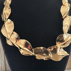 Pu&ograve; includere: Una collana dorata con un design a foglie. La collana &egrave; composta da molteplici elementi sovrapposti a forma di foglia e strutturati. Le foglie hanno una finitura metallica riflettente e sono disposte in una catena continua.
