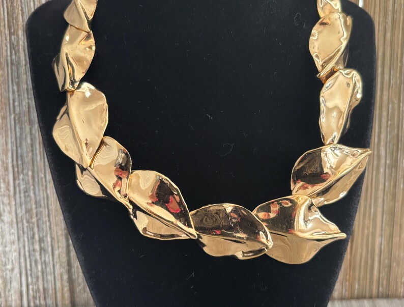 Pu&ograve; includere: Una collana dorata con un design a foglie. La collana &egrave; composta da molteplici elementi sovrapposti a forma di foglia e strutturati. Le foglie hanno una finitura metallica riflettente e sono disposte in una catena continua.