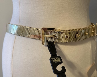 May include: A gold-toned chain belt with a square buckle. The belt is made of small, linked metal squares. The buckle has a small, round hole on each side.