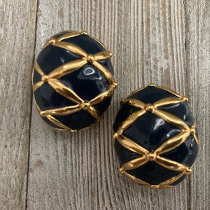 May include: A pair of clip-on earrings in gold and navy blue. The earrings are round and feature a geometric design.