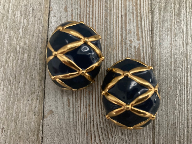May include: A pair of clip-on earrings in gold and navy blue. The earrings are round and feature a geometric design.
