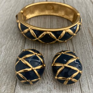 May include: A gold and navy blue bracelet and matching earrings. The bracelet is a wide bangle with a geometric pattern. The earrings are round and have the same geometric pattern as the bracelet.