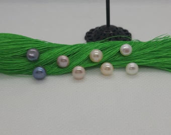 Peut inclure: Sept perles rondes de différentes couleurs, dont le blanc, le rose et le gris, sont disposées sur une surface en tissu vert.