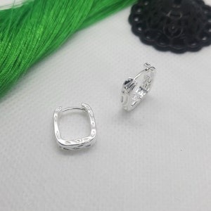 May include: A pair of silver hoop earrings with a textured, square design.
