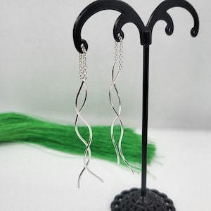 May include: A pair of silver dangle earrings with a twisted wire design and a delicate chain.