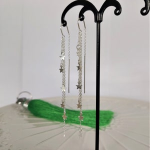 May include: Silver dangle earrings with multiple chains and star charms. The earrings are hanging from a black earring stand.