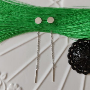Op de afbeelding: Een paar zilveren oorhangers met kleine ronde schijven aan de bovenkant en een dunne zilveren staaf aan de onderkant.