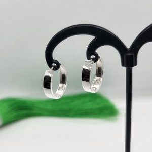 Może przedstawiać: Para srebrnych kolczyków koła. Kolczyki są gładkie i mają polerowane wykończenie.