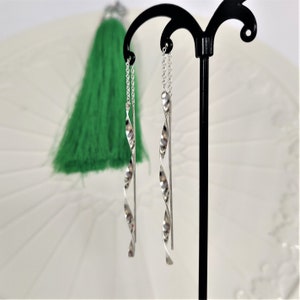 May include: A pair of silver dangle earrings with a twisted design. The earrings are hanging from a black stand.