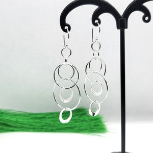 May include: Silver dangle earrings with multiple interconnected circles. The earrings are hanging from a black earring stand.