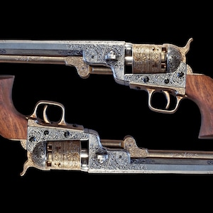 May include: Two antique silver and gold revolvers with intricate engravings and wooden grips. The revolvers are displayed against a black background.