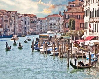 May include: A view of the Grand Canal in Venice, Italy, with gondolas and boats docked along the sides. The canal is lined with colorful buildings and bridges.