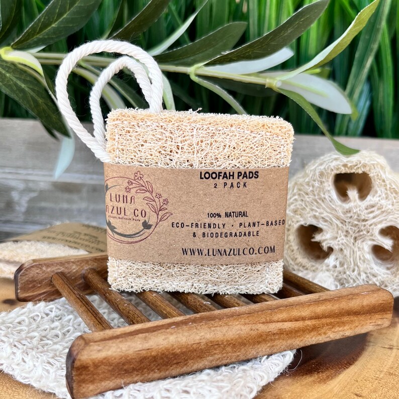 May include: Two natural loofah pads in a 2-pack, with a brown paper label that reads "Loofah Pads 2 Pack 100% Natural Eco-Friendly Plant-Based & Biodegradable www.lunazulco.com".