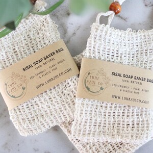 May include: Two off-white sisal soap saver bags with wooden bead accents. Each bag has a brown label with the text "SISAL SOAP SAVER BAG 100% NATURAL" and the Luna Azul Co. logo. The bags are eco-friendly and plant-based.