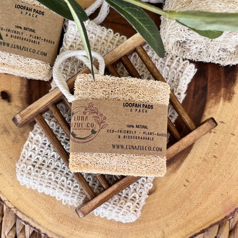 May include: Two natural loofah pads on a wooden soap dish. The loofah pads are eco-friendly, plant-based, and biodegradable. The packaging says "Loopah Pads 2 Pack 100% Natural Eco-Friendly Plant-Based & Biodegradable www.lunazulco.com"