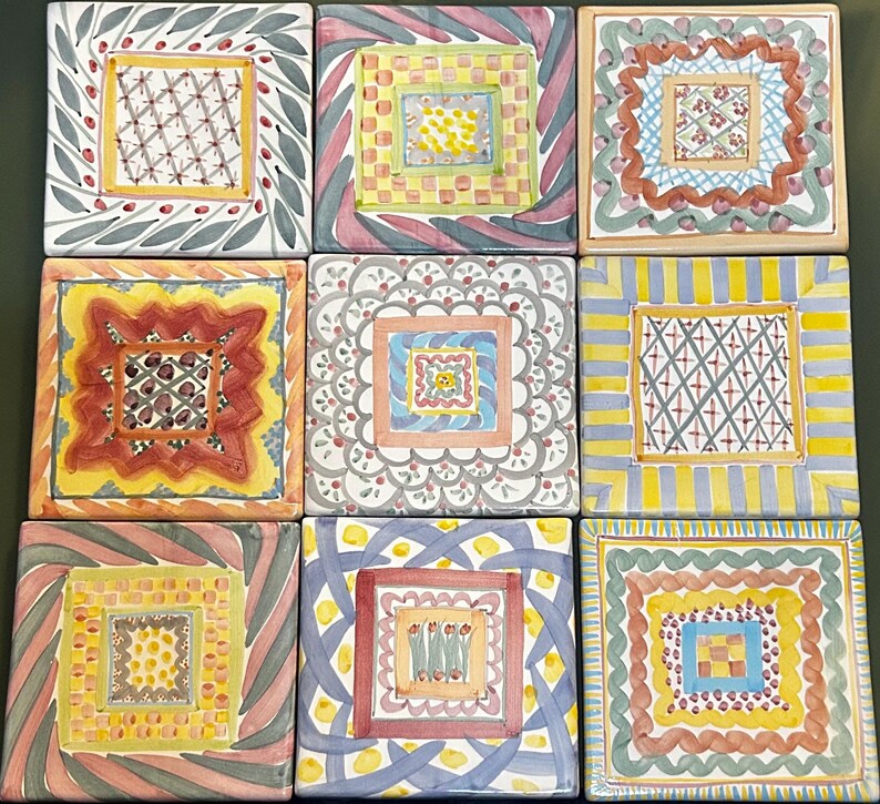 Może przedstawiać: Dziewięć kwadratowych płytek ceramicznych z ręcznie malowanymi wzorami. Każda płytka ma centralny kwadrat otoczony skomplikowanymi wzorami i obramowaniami w r&oacute;żnych kolorach, w tym ż&oacute;łtym, niebieskim, czerwonym i zielonym. Płytki ułożone są w siatkę 3x3.