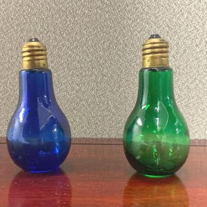May include: Two glass lightbulb shaped bottles, one blue and one green. The bottles have a gold metal top.