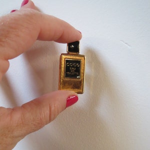 Könnte beinhalten: Eine goldfarbene Miniatur-Parfümflasche mit schwarzem Verschluss und Etikett. Das Etikett trägt die Aufschrift "COCO EAU DE TOILETTE".