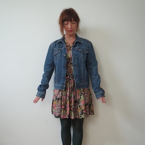 May include: A woman wearing a floral print dress, a denim jacket, dark green tights, and brown ankle boots.