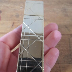 May include: A gold-colored rectangular lighter with a geometric pattern of intersecting lines. The lighter is held in a hand, and the background is a wooden surface.