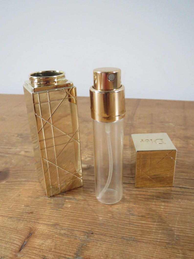 May include: A gold-colored perfume atomizer and case set. The atomizer is clear with a gold cap. The case is rectangular with a geometric design. A small gold box with the word "Dior" is also included.