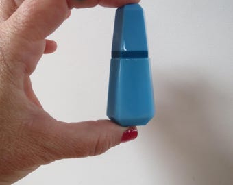 May include: A light blue, geometric-shaped bottle. The bottle has a faceted design and a matching cap. The object is held between fingers against a white background. The bottle is approximately 4 inches tall.