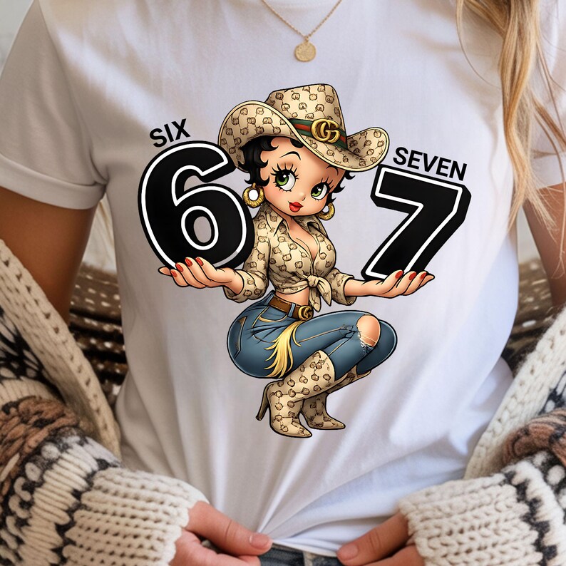 May include: White t-shirt featuring a cartoon cowgirl holding the numbers 6 and 7. The cowgirl wears a patterned cowboy hat, a button-down shirt, blue jeans with a ripped knee, and cowboy boots. The words "SIX" and "SEVEN" are above the numbers.