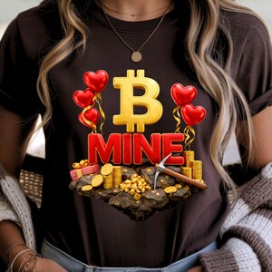 May include: A dark brown t-shirt featuring a gold Bitcoin symbol and the word "MINE" in red. Red heart-shaped balloons, gold coins, and a pickaxe are also depicted, creating a cryptocurrency-themed design.
