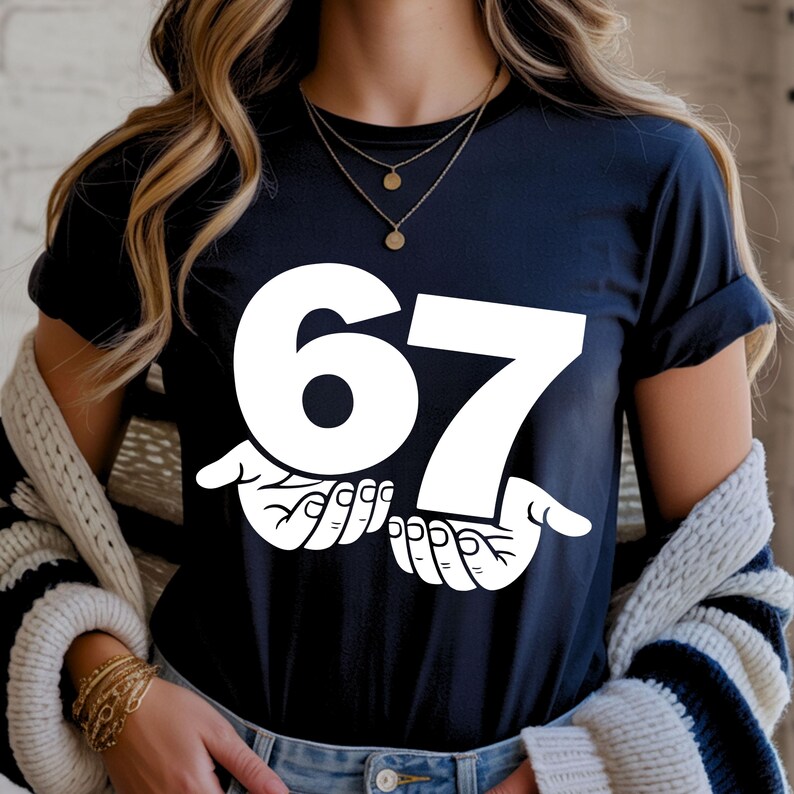 Puede incluir: Una camiseta azul marino con el n&uacute;mero "67" en letras blancas grandes, sostenida por dos manos blancas. La camiseta tiene mangas cortas y cuello redondo.