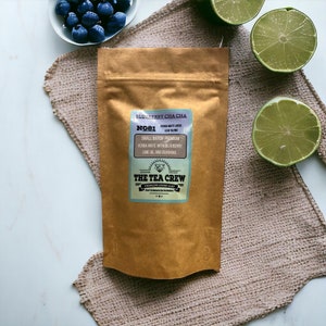 May include: A brown paper bag with a label that says "Blueberry Cha Cha" and "The Tea Crew" with a small illustration of a teacup and a tea bag. The label also says "Yerba Mate Loose Leaf Blend" and "Small Batch Premium Yerba Mate with Blueberry, Lime Oil and Guarana".