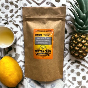 May include: A brown paper bag with a label that says "Amazonian Queen" and "N080 Yerba Mate Loose Leaf Blend". The label also says "Small Batch Premium Yerba Mate with Pineapple, Mango and Lemon." The label has a logo with a cat and the words "The Tea Crew Premium Loose Leaf".