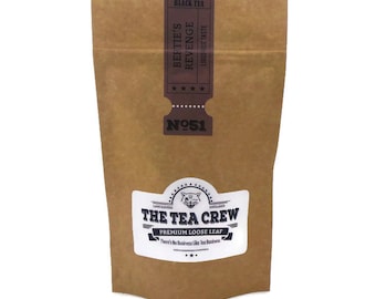 May include: A brown paper bag with a white label that says "The Tea Crew Premium Loose Leaf" and a black and white illustration of a cat. The label also says "There's No Business Like Tea Business". The bag has a black and white label with the text "Black Tea Bef Tie's Revenge Liquorice Taste" and "N051".