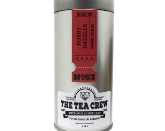 Può includere: Una scatola di metallo argentata con un'etichetta rossa che dice "Bobby Dazzler Yorkshire Tea Blend" e "Nº53". L'etichetta presenta anche un'illustrazione in bianco e nero di un gatto con il testo "The Tea Crew Premium Loose Leaf There's No Business Like Tea Business".