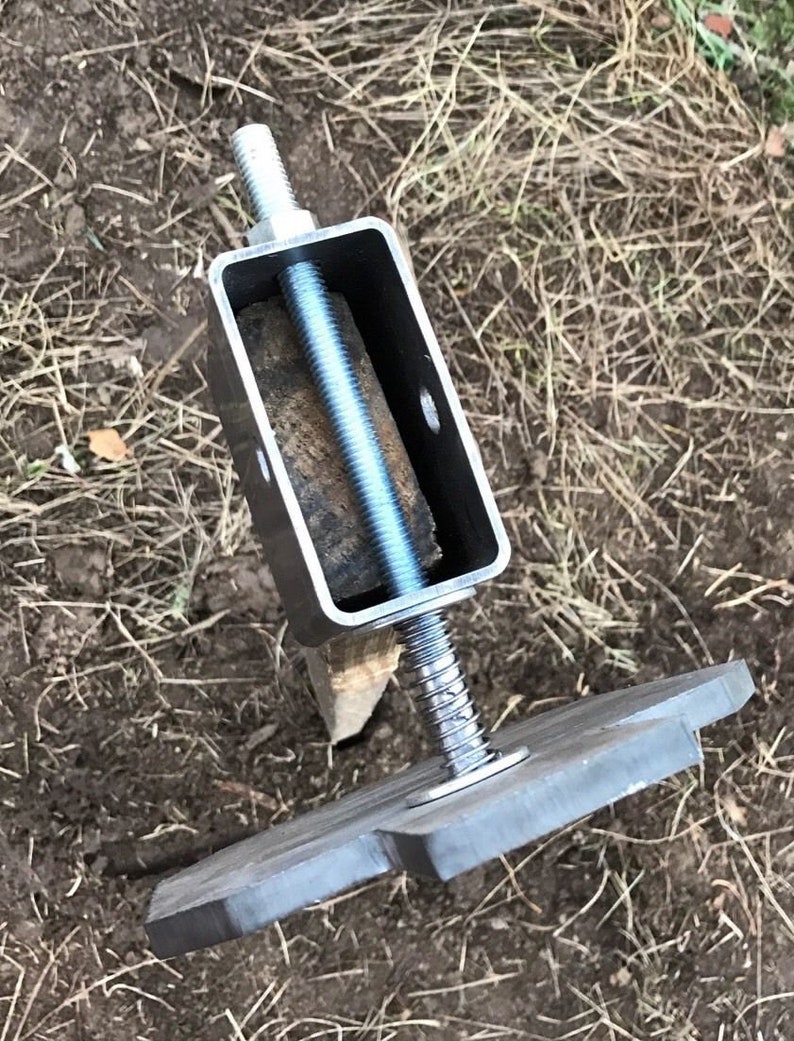 May include: A metal post support with a threaded rod and a square base plate. The rod is threaded through a metal bracket and secured with a nut. The base plate has a star-shaped design.