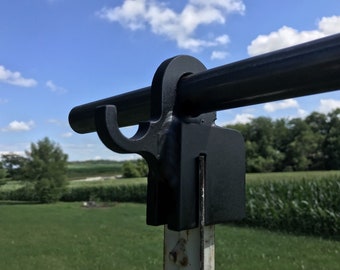 May include: Black metal gate hook with a rounded top and a hook on the side. The hook is attached to a black metal pipe.