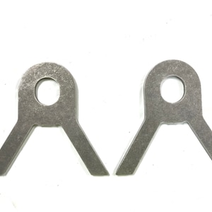 May include: Two silver metal brackets with a round hole in the center and two angled arms. The brackets are designed for mounting or attaching objects.